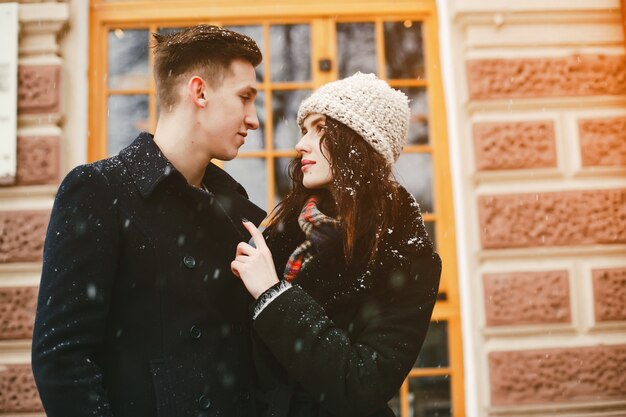 elegante casal apaixonado em casacos pretos andando na cidade de neve de inverno