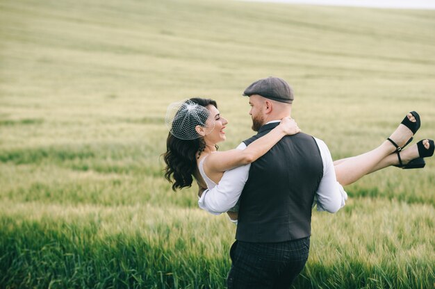 Elegante casal de noivos em um campo verde perto de carro retrô.