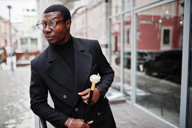 Elegante cavalheiro afro-americano na elegante jaqueta preta segurando a bengala retrô como balão de cana ou bengala com alça de bola de diamante dourado Rico homem afro elegante