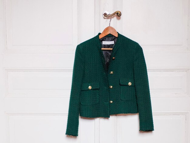 Elegante chaqueta verde de moda para mujer con grandes botones dorados cuelga de una percha de madera