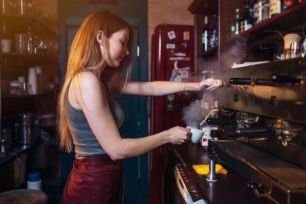 Elegante chica de jengibre haciendo café con una máquina profesional