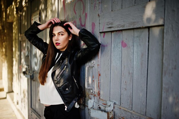 Elegante chica morena vestida con chaqueta de cuero y pantalones cortos posando en la calle