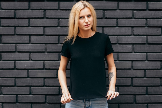 Elegante chica rubia con camiseta negra posando sobre fondo de pared negra