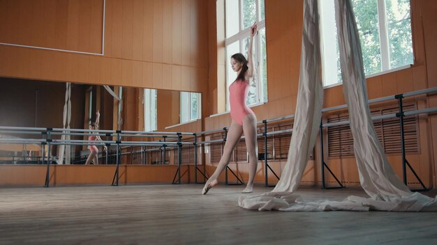 Elegante chica en vestido rosa y zapatos de punta bailarina practicando en el estudio, elementos de danza, telefoto