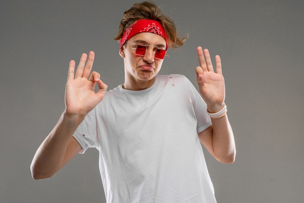 elegante chico rubio con un pañuelo en gafas y una camiseta blanca muestra bien en una pared gris