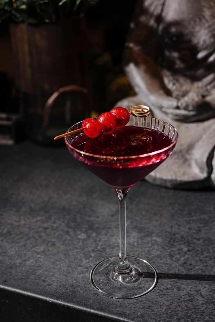 Elegante cóctel con guarnición de cerezas servido en un elegante vaso en una encimera oscura en un bar por la noche