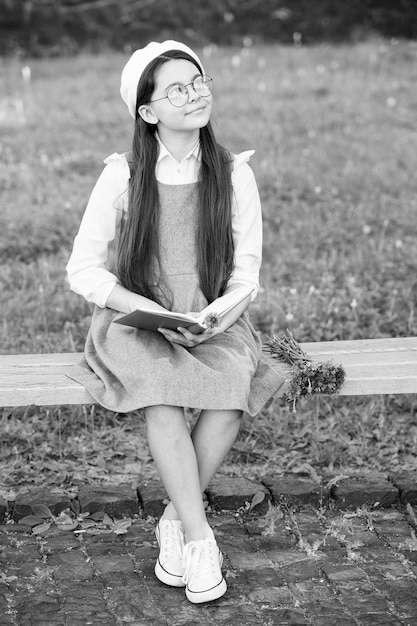 Elegante colegiala niña leyendo un libro en el parque aprende el concepto de gramática