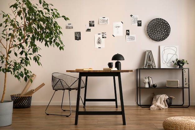 La elegante composición del acogedor interior de la oficina con una silla de metal, una mesa de madera, un póster de plantas y accesorios personales. Plantilla de decoración del hogar.