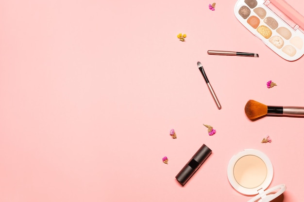 Foto elegante composición plana sobre un fondo rosa con flores con productos de maquillaje