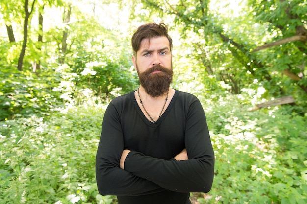 Elegante y confortable. Hipster con estilo serio en verano al aire libre. Hombre barbudo con cabello elegante vistiendo camiseta casual en día soleado. Modelo de moda brutal manteniendo los brazos cruzados con estilo.