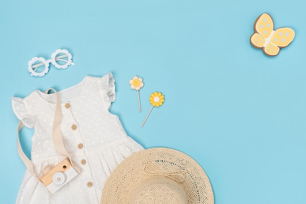Elegante conjunto de ropa de verano para niños Vestido blanco, sombrero de paja, gafas de sol y accesorios sobre fondo azul Concepto de lookbook de chica de moda Vista superior Copiar espacio Plano
