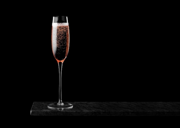 Elegante copa de champán rosa rosa con burbujas en tablero de mármol negro sobre negro