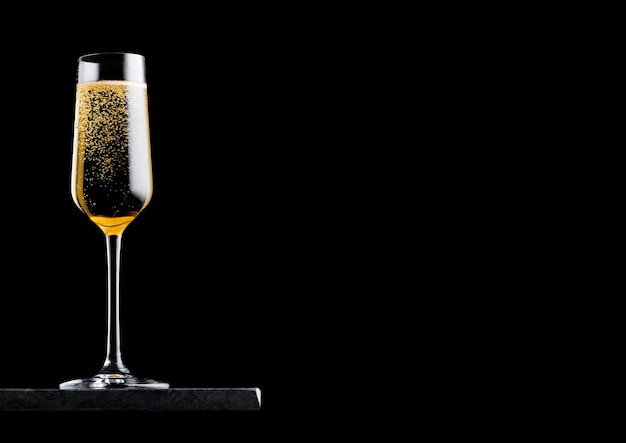 Elegante copo de champanhe amarelo com bolhas na placa de mármore preto sobre fundo preto