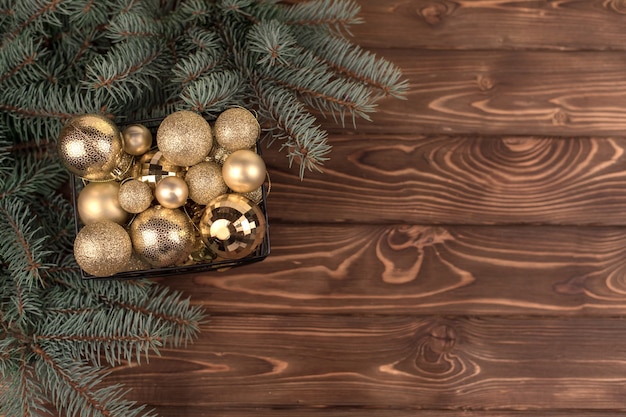 Elegante cubo de juguetes de Navidad dorados sobre un fondo de madera blanca y ramas de árboles de Navidad