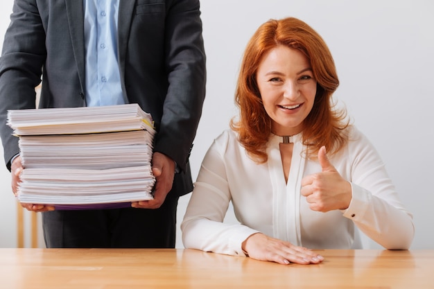 Elegante dama admirable hermosa sentada en su lugar de trabajo y con una pila de documentos entregados para su consideración