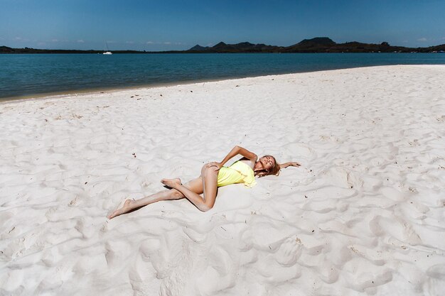 Elegante dama adulta con una atractiva figura sexy y piernas largas tumbada en la arena de una playa local y tomando el sol en un caluroso día de verano. Concepto de vacaciones.