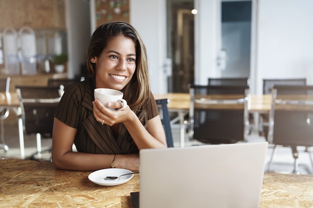 Elegante dama de oficina guapa disfrutando de café caliente sosteniendo la taza sitttin en el café solo