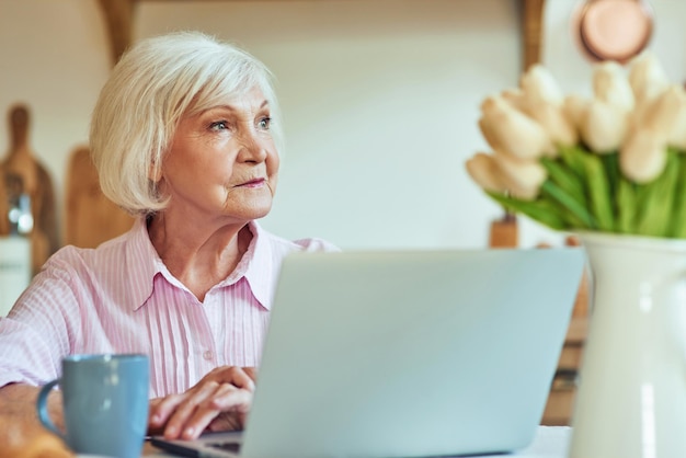 Elegante dama de pelo gris usando la computadora en casa