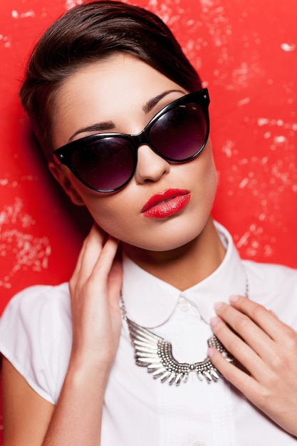 Elegante e bonito. Mulher jovem e bonita de cabelo curto em camisa branca posando contra um fundo vermelho