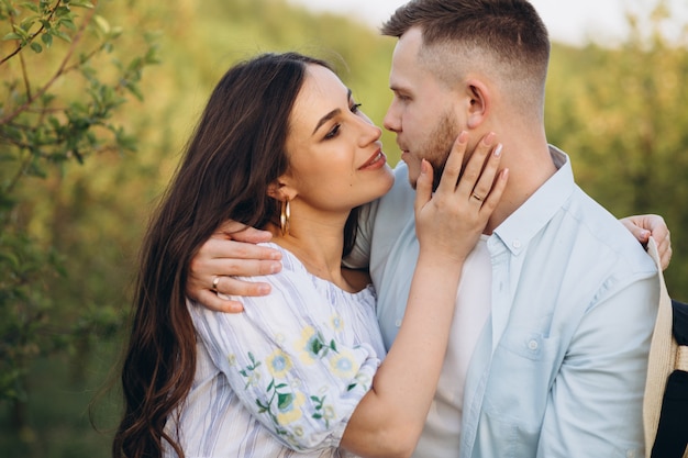 Elegante e elegante mulher grávida e seu marido vestiram um tom branco e azul pastel no jardim por do sol