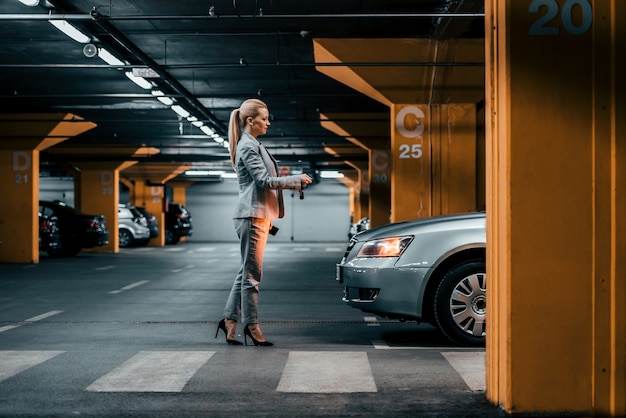 Foto elegante empresaria con las llaves del auto frente a un auto en un estacionamiento subterráneo.