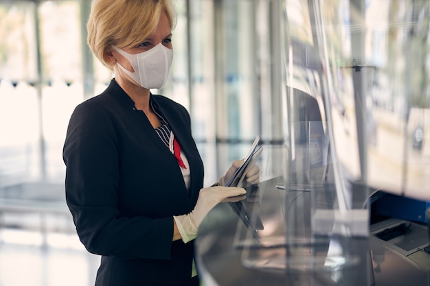 Elegante empresaria en mascarilla protectora y guantes estériles con smartphone y billete de avión