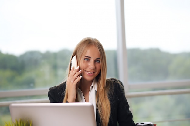 Elegante empresaria sentada en su oficina y hablando por teléfono