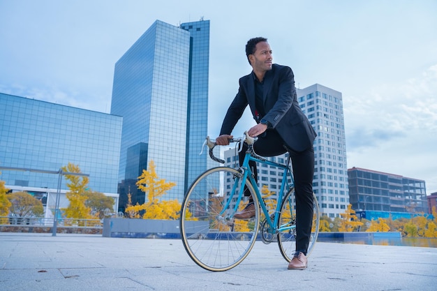 Elegante empresário afro-americano de terno indo para o escritório de bicicleta no distrito financeiro