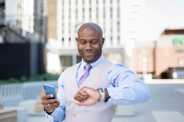 Elegante empresario afroamericano mirando la hora en su reloj mientras sonríe.