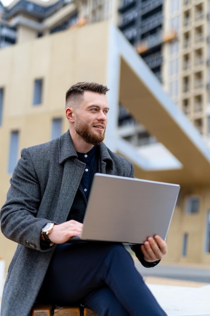 Elegante empresário bonito trabalhando com laptop na rua Jovem atraente em pano casual na rua urbana