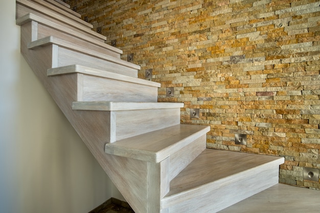 Elegante escalera contemporánea de madera en el interior de la casa loft. Pasillo moderno con paredes decorativas de piedra caliza y escaleras de roble blanco.