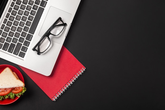 Elegante escritorio de oficina negro con laptop, taza de café y un sándwich para el almuerzo. Vista superior con espacio de copia.