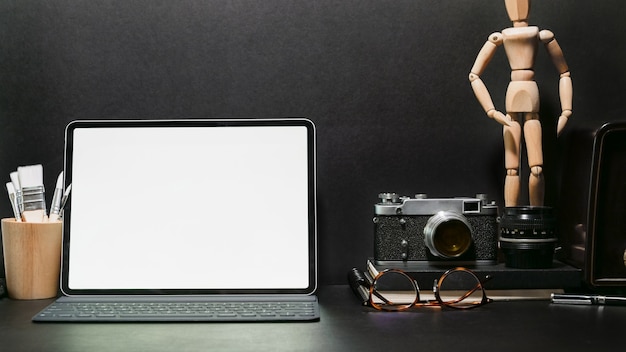 Elegante escritorio de trabajo, cámara vintage, tableta de pantalla en blanco y dispositivo en mesa de cuero oscuro