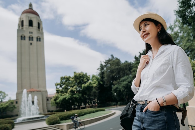 elegante estudiante estudiar en el extranjero universidad en america stanford. joven universitaria sonriendo con la iglesia de la torre en segundo plano en verano. hombre montando en bicicleta en la carretera en el parque al aire libre con árboles y plantas.