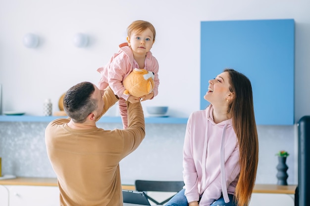 Elegante familia feliz divirtiéndose en casa en la cocina Los padres juegan con su bebé papá levanta a la niña en sus brazos