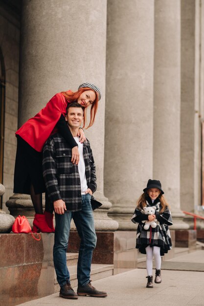 Una elegante familia de tres pasea por la ciudad otoñal posando para un fotógrafo Papá, mamá e hija en la ciudad otoñal