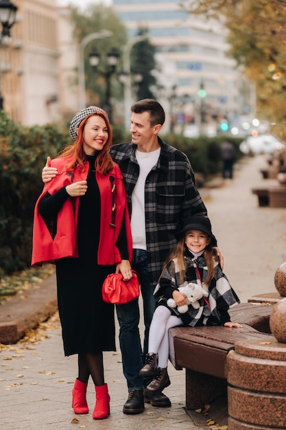 Una elegante familia de tres pasea por la ciudad otoñal posando para un fotógrafo Papá, mamá e hija en la ciudad otoñal