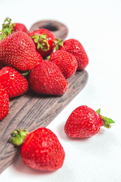 Elegante fondo de fresa tierna. Bayas rojas maduras de verano. Bayas dulces para el desayuno de la mañana o bayas para el postre. Fresas enteras sobre tabla de madera y fondo blanco.