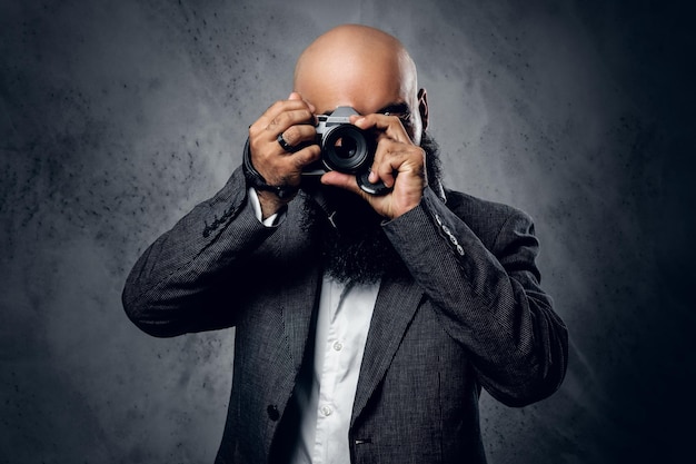 Elegante fotógrafo profesional barbudo en traje de tiro con una cámara réflex digital compacta.