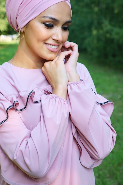 Elegante Frau im rosa Turban, die zwischen den Bäumen lächelt.