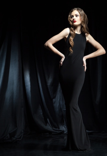 Elegante Frau im schwarzen Kleid mit Armen auf den Hüften