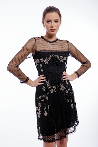 Elegante Frau im schwarzen Kleid mit Spitze posiert auf weißem Hintergrund