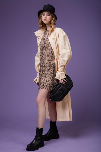 Elegante Frau in beigem, cremefarbenem Trenchcoat, braunem Kleid mit einer schwarzen Hutstiefelhandtasche mit Blumenmuster