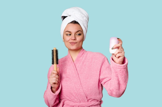 Foto elegante frau in einem rosafarbenen bademantel bereit für den tag mit haarbürste und deodorant in der hand