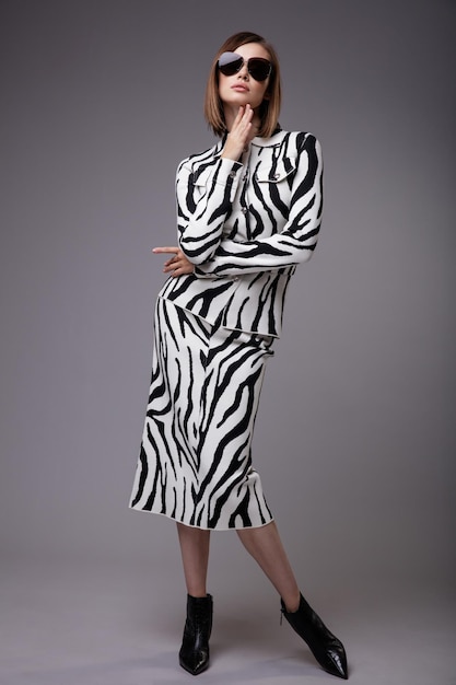 Elegante Frau in hübschem Zebra-Print Anzug Jacke Rock schwarze Stiefeletten Sonnenbrille grauer Hintergrund