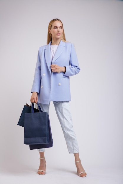 elegante frau in hübschen blauen jeans, jacke auf weißem hintergrund, einkaufstüten