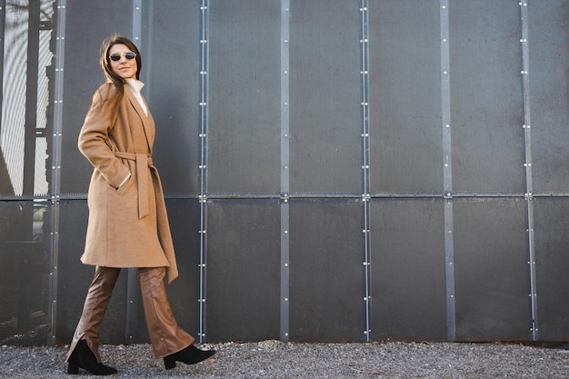 Elegante Frau in Mantel und Sonnenbrille geht spazieren