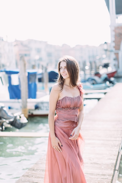 Una elegante y gentil niña sonriente con un largo vestido rosa caminando en Venecia.