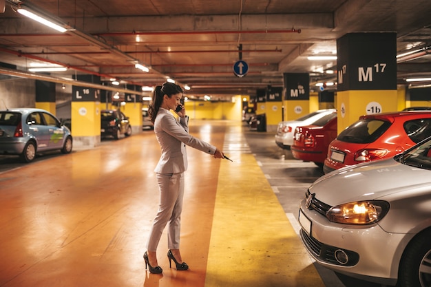 Elegante Geschäftsfrau, die ihr Auto mit Schlüsseln in der Tiefgarage abschließt.