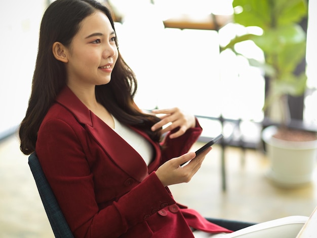 Elegante Geschäftsfrau sitzt an ihrem Schreibtisch und verwendet ein modernes Smartphone, um sich mit dem Internet zu verbinden